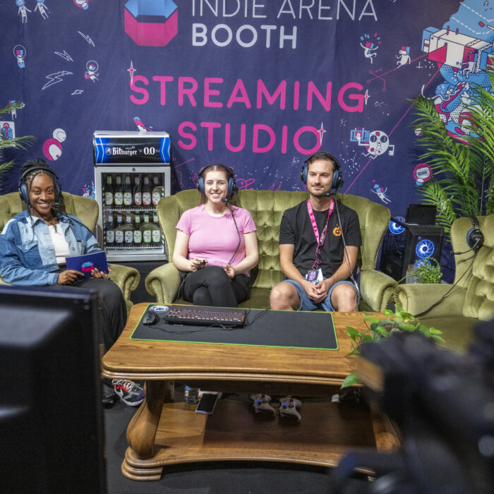 Foto vom Indie Arena Booth Streaming Studio in dem 3 Personen auf einer Couch sitzen und spielen. Foto: Koelnmesse / gamescom