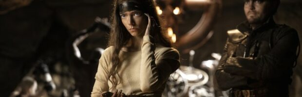 Szene aus dem Film Furiosa. Eine junge Frau mit langen Haaren steht vor einem Altar aus Lenkrädern