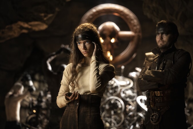Szene aus dem Film Furiosa. Eine junge Frau mit langen Haaren steht vor einem Altar aus Lenkrädern