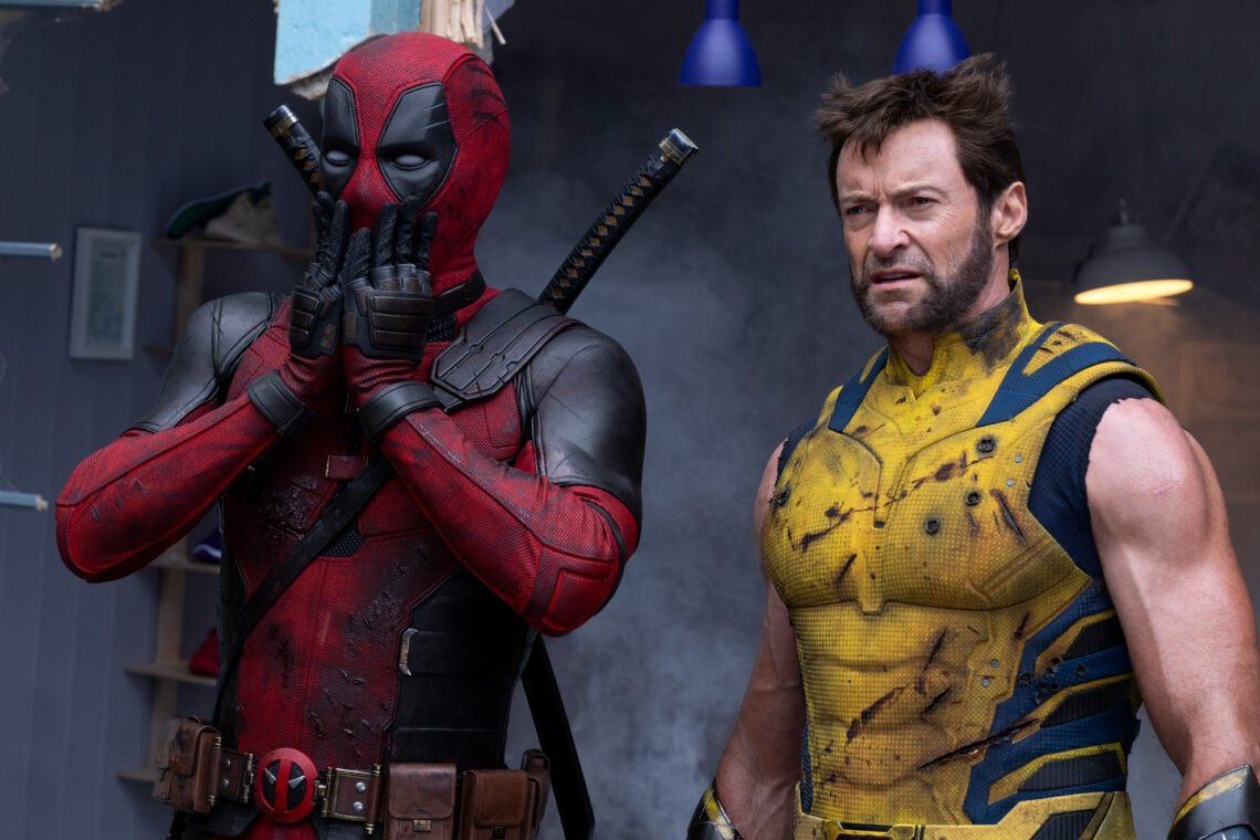 Szene aus dem Deadpool & Wolverine Film. Links steht Deadpool in rot-schwarzem Anzug und hält sich erschrocken die Hände vor den Mund. Rechts steht Wolverine in gelb-blauem Anzug und sieht verwirrt aus.