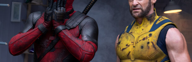 Szene aus dem Deadpool & Wolverine Film. Links steht Deadpool in rot-schwarzem Anzug und hält sich erschrocken die Hände vor den Mund. Rechts steht Wolverine in gelb-blauem Anzug und sieht verwirrt aus.