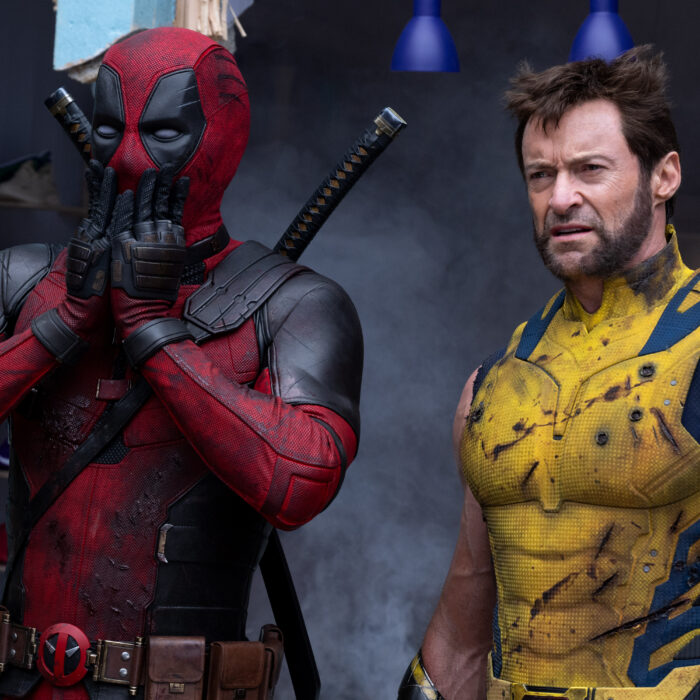 Szene aus dem Deadpool & Wolverine Film. Links steht Deadpool in rot-schwarzem Anzug und hält sich erschrocken die Hände vor den Mund. Rechts steht Wolverine in gelb-blauem Anzug und sieht verwirrt aus.